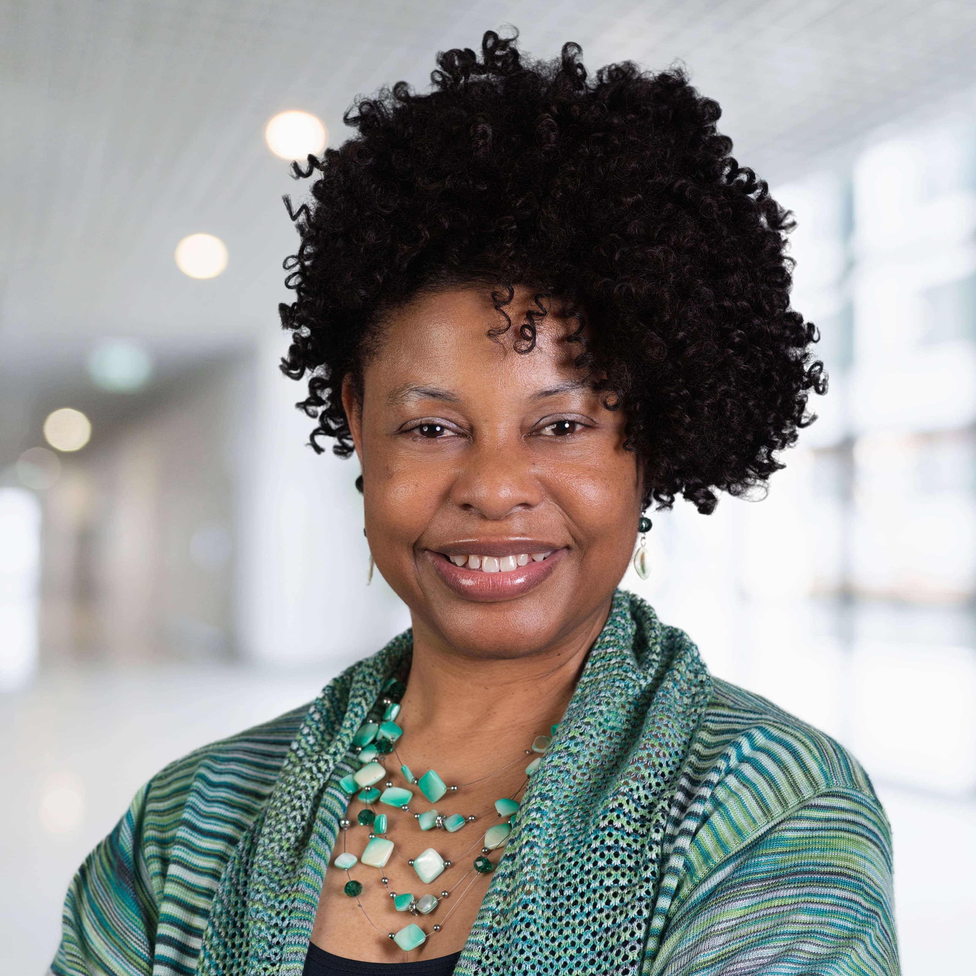 A smiling Black woman with short, curly hair wearing a green patterned cardigan and necklace.